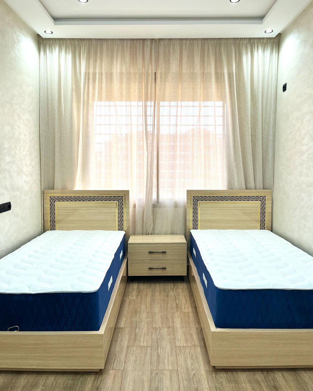 Chambre à coucher avec deux lits simples en MDF finition bois et table de chevet centrale – BOALUM