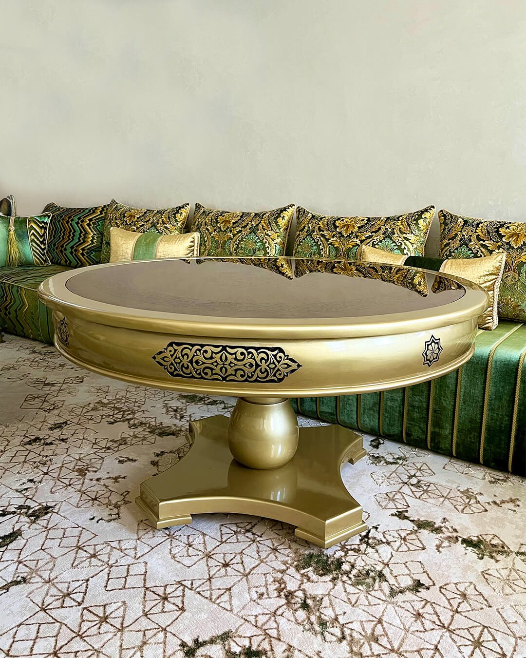 Table centrale de salon marocain dorée en bois sculpté, vue latérale, avec plateau rond et base élégante.